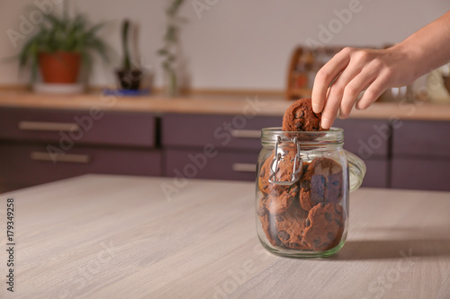 Billede på lærred Woman taking oatmeal cookie with chocolate chips from glass jar