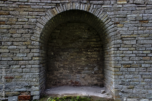 Stone brick antique arch is a window. Northern Europe, the castle. Fortress wall made of gray bricks.