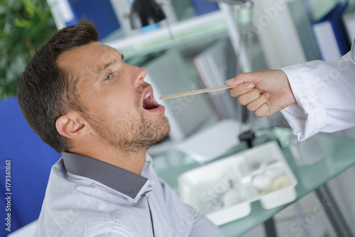 doctor examines middle aged man for sore throat