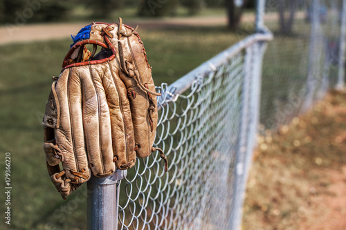 Slika na platnu An old scuffed leather baseball glove hanging on the post of a chain link fence