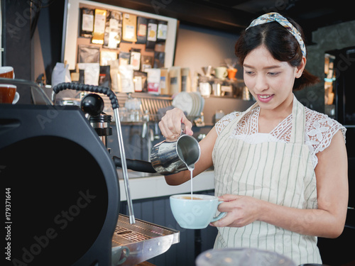 Asian young woman barista brewing coffee using coffee machine.
