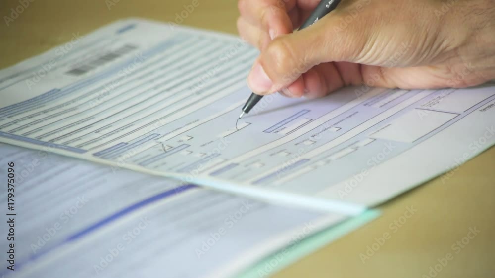 Close-up of a hand of a man completing an official form and signing it. A man filling in a document Close-up of a hand of a man completing an official form and signing it. A man filling in a document