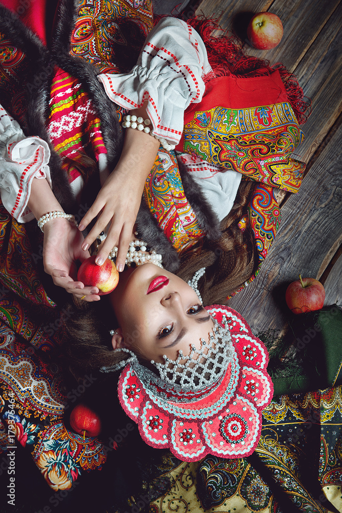The girl in the folk style and bright make-up holding an Apple on dark wooden background top view
