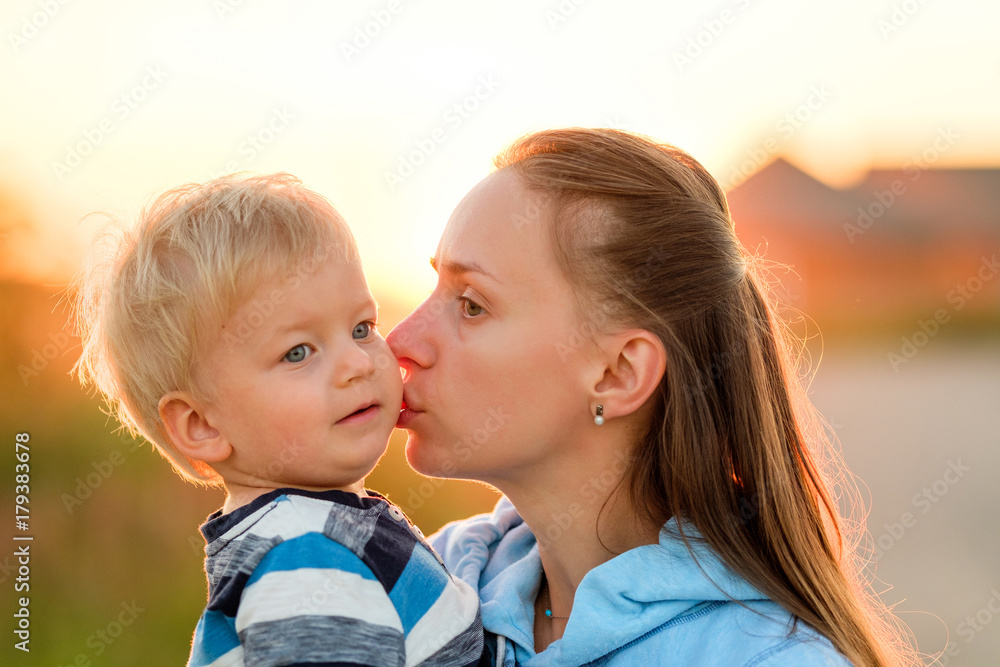 Woman and child outdoors at sunset. Mother kissing her son. Woman and child outdoors at sunset. Mother kissing her son.