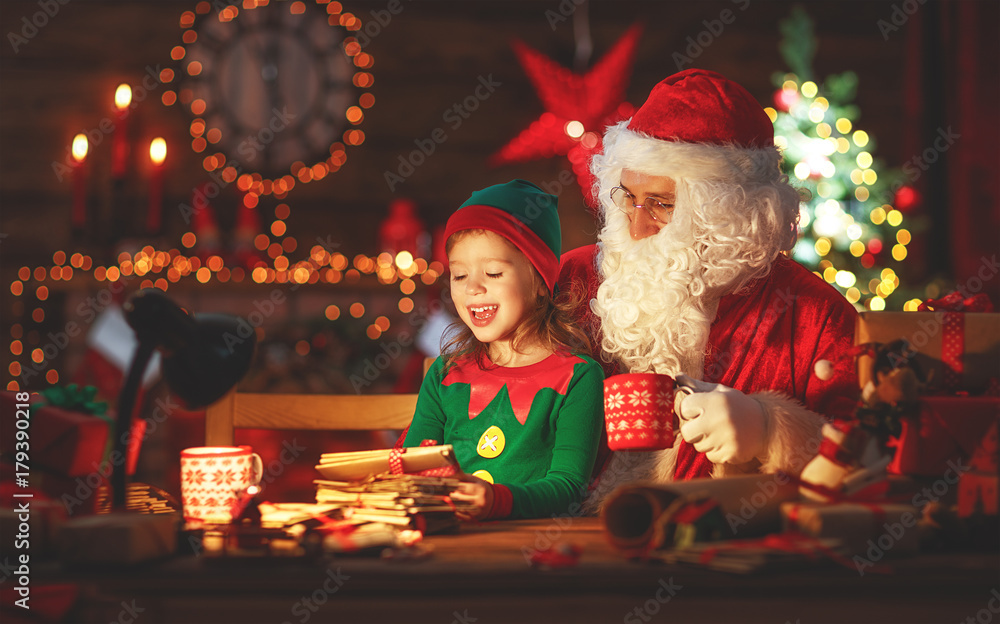 santa claus reads letter to little elf by Christmas tree santa claus reads letter to little elf by Christmas tree