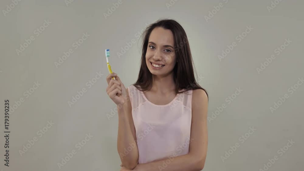 Attractive millennial girl smiling holding toothbrush. Portrait happy beautiful model wearing casual shirt Attractive millennial girl smiling holding toothbrush. Portrait happy beautiful model wearing casual shirt