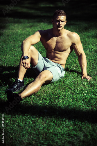 Man sportsman with muscular body sit on green grass