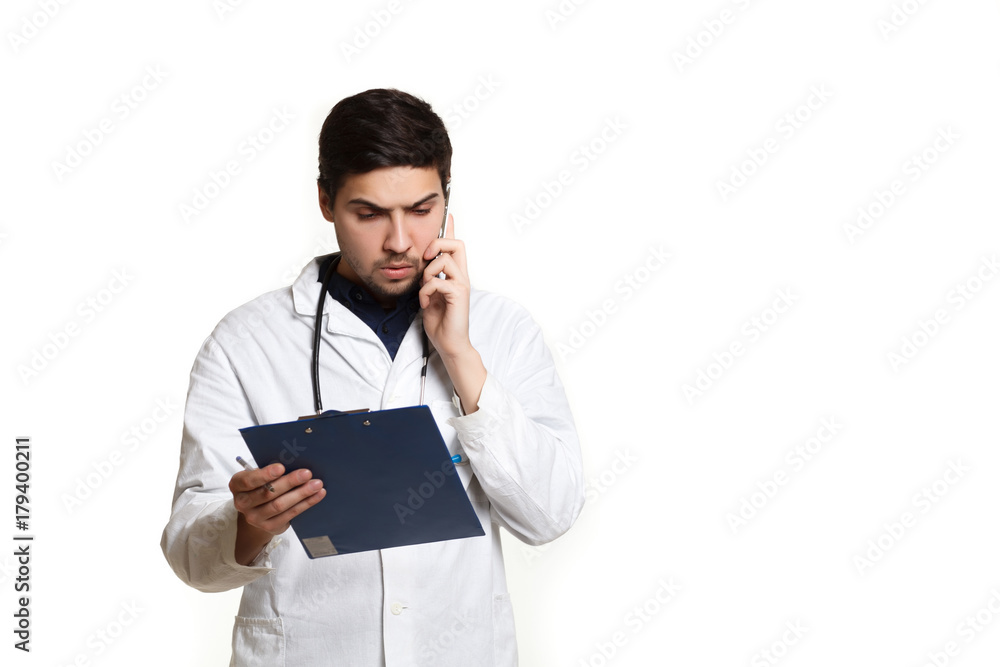 beautiful young doctor in a dressing gown with a stethoscope on a white background in the studio, records a medical history, talking on the phone beautiful young doctor in a dressing gown with a stethoscope on a white background in the studio, records a medical history, talking on the phone