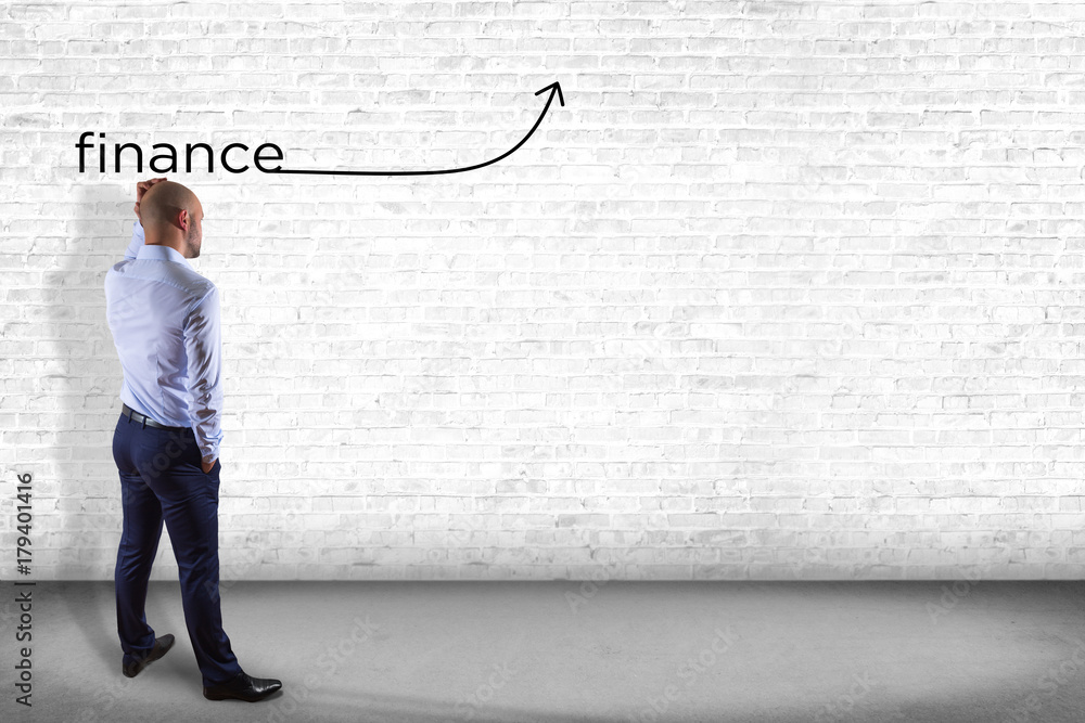 Businessman in front of a wall thinking about the word finance with a arrow - business concept Businessman in front of a wall thinking about the word finance with a arrow - business concept