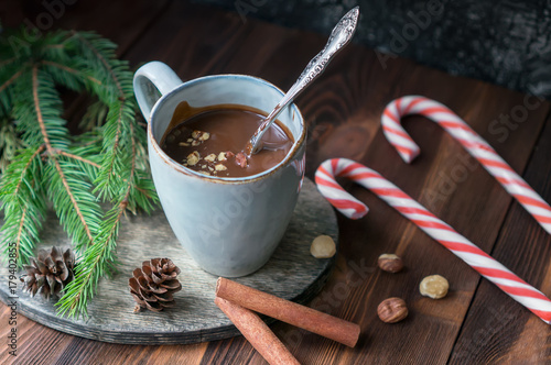 Cup of hot chocolate with hazelnuts and cinnamon sticks on wooden table. Sweet candy canes, fir branches and cones decoration. Christmas holiday background.  photo
