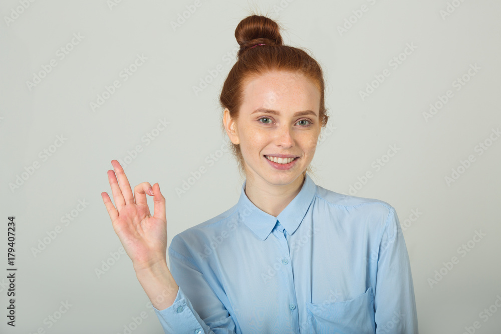 beautiful young smiling girl with red hair on a light background with an approving hand gesture beautiful young smiling girl with red hair on a light background with an approving hand gesture