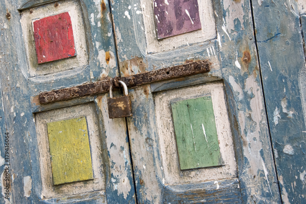 Brightly coloured flaky pain in blue, yellow, red, purple and green on old window shutters secured with a rusting bolt and padlock. Shot as a Dutch tilt in the Souk in Essaouira,Morocco Brightly coloured flaky pain in blue, yellow, red, purple and green on old window shutters secured with a rusting bolt and padlock. Shot as a Dutch tilt in the Souk in Essaouira,Morocco
