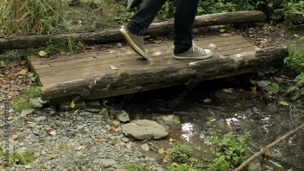 male feet walk along the wooden bridge across the stream male feet walk along the wooden bridge across the stream