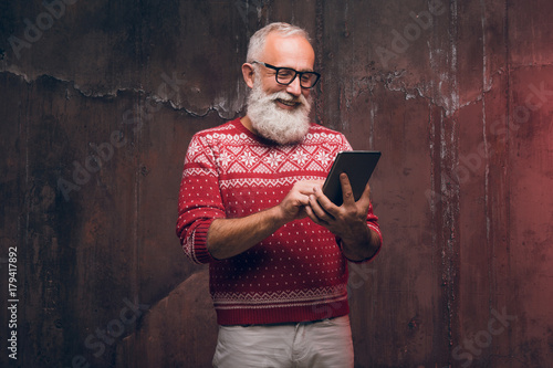 A modern happy senior man using a smartphone in a Christmas sweater. Santa Claus wishes Merry Christmas