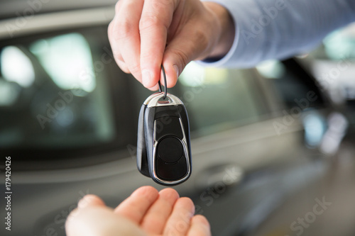 close up photo of male hand giving car keys to female hand, indoors in car dealership