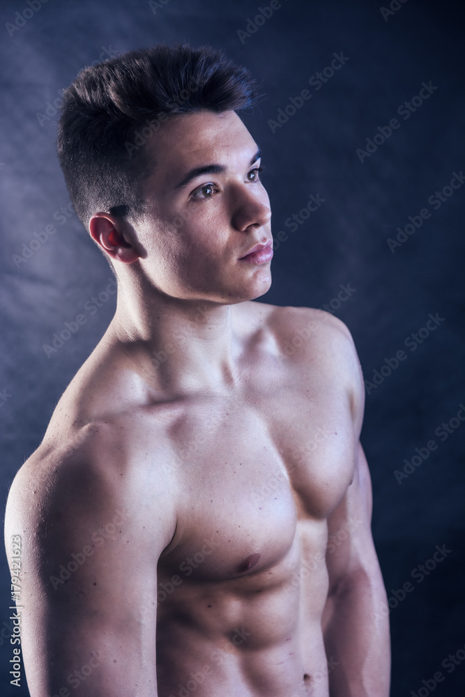 Handsome young muscular man shirtless wearing jeans, on dark background in studio shot