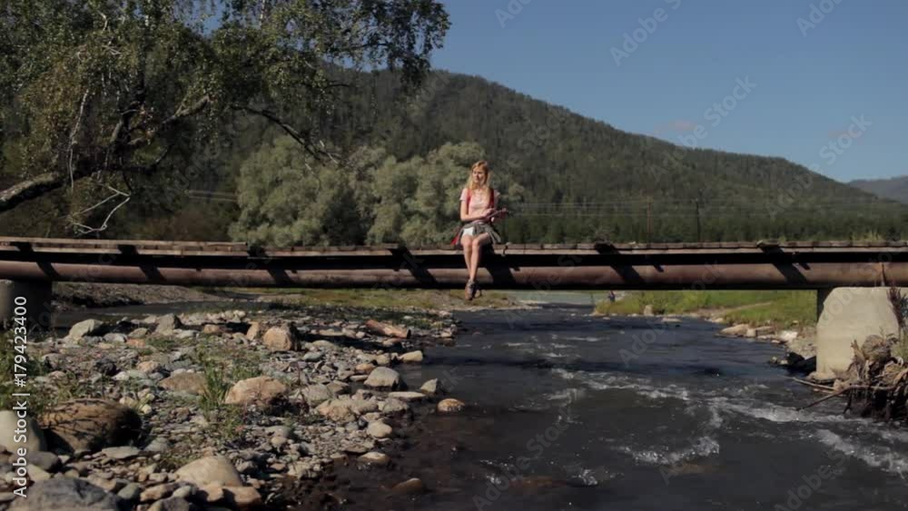 girl traveler with a tablet sits on a bridge across a mountain river girl traveler with a tablet sits on a bridge across a mountain river