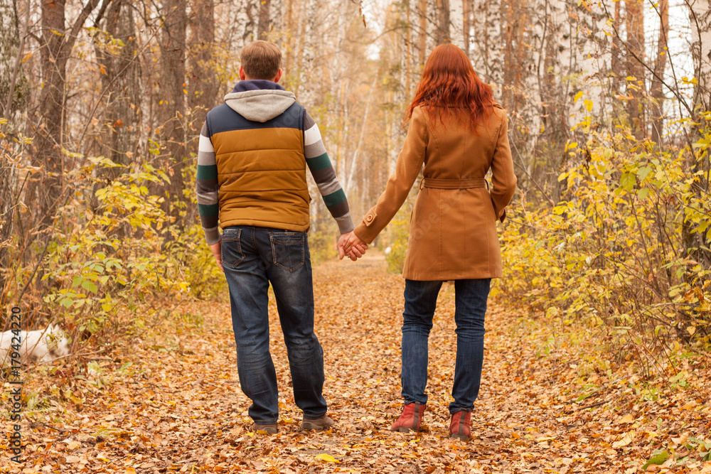 Couple holding hands and standing by their backs. Man and woman walking outdoor in autumn park. Love and romantic lesure activity