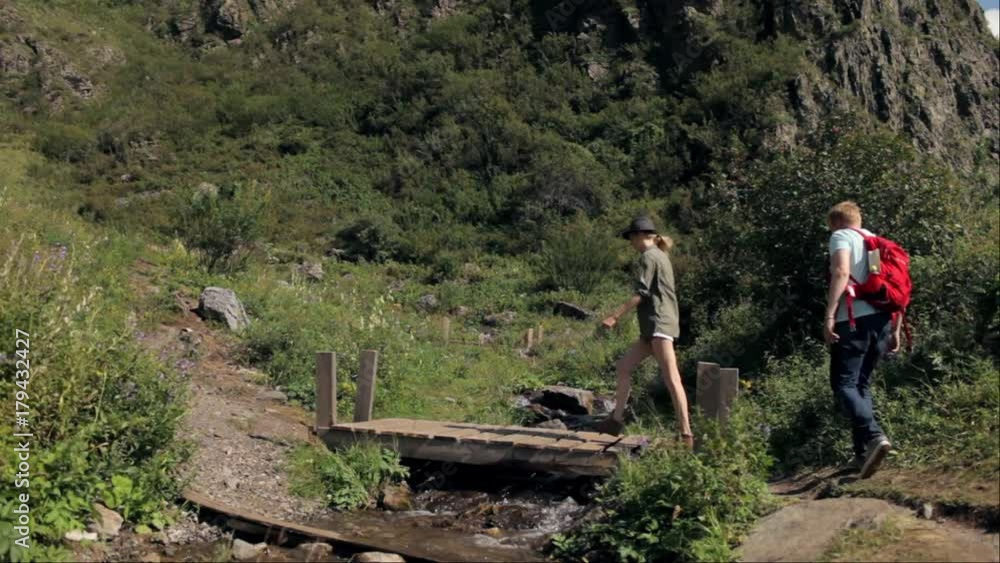 young couple of travelers pass a mountain stream young couple of travelers pass a mountain stream