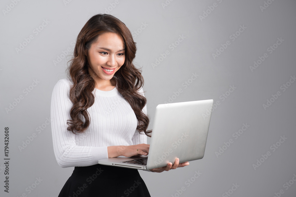 Portrait of a smiling asian woman holding laptop computer isolated on gray background Portrait of a smiling asian woman holding laptop computer isolated on gray background