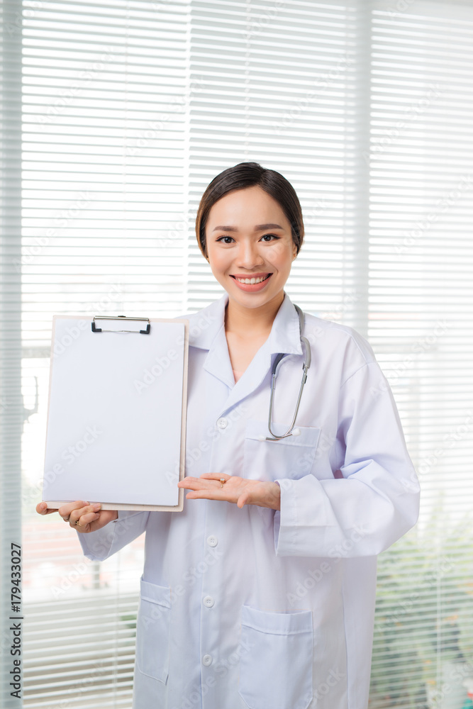Asian young female doctor upset point to blank clipboard while standing at hospital Asian young female doctor upset point to blank clipboard while standing at hospital