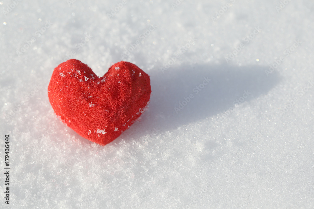 On the snow lies a red heart made of foam rubber. Template for a holiday card with a white texture and free space for text.