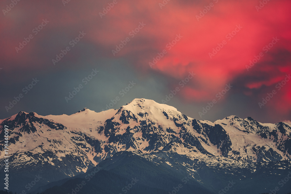 Beautiful sunset over the snowy mountain peak. Nature landscape scene. Dramatic overcast red sky. Holidays, travel, sport, recreation. Main Caucasian ridge, Svaneti, Georgia. Retro toning filter