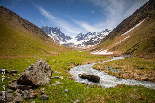 Summer landscape with river and mountain snowy peak, Kazbegi national park, Georgia. The main Caucasian ridge. Green hills and small mountain river in Caucasus foothills, above view