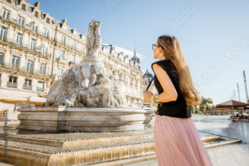 Young woman tourist standing with photo camera on the Comedy square with main fountain on the background in Montpellier city, France