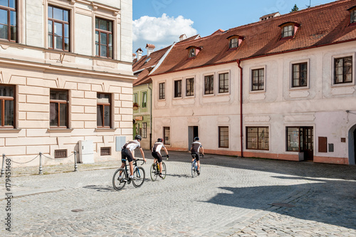 A group of cyclists rides around town on a Sunny day on the cobbled road.