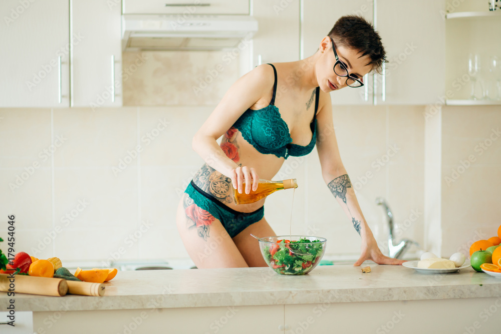 Kitchen. Sexy girl in lingerie pours oil in salad Stock Photo | Adobe Stock