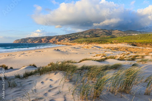 Sunny beach with sand dunes and blue sky and a mountain in background. Guincho beach in Cascais Portugal