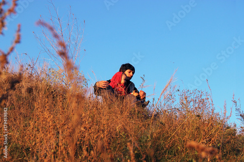 The child and father sit on a hill in a thick dry grass. Autumn picnic in nature. Happy family father and daughter playing with dad high grass meadow on sunset. A child of one two years and a parent