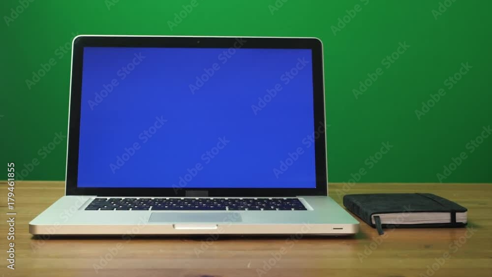 Laptop with a green screen and black notepad on table. Green screen background Laptop with a green screen and black notepad on table. Green screen background