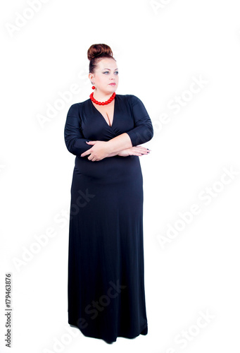 Beautiful confident buxom woman in black evening dress in full, with red costume jewelry stands isolated in full growth on a white background