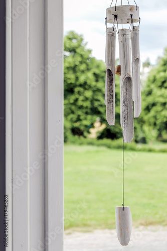Fotografie white wooden wind chime hang on window with green garden