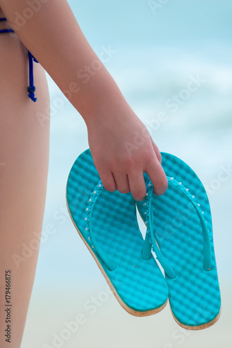 blue flip flops in the hand of a girl on the beach close-up