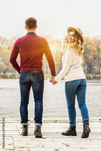Forever together. Rear view of beautiful young couple in casual clothing keeping hands together while walking outdoors. Woman looking to camera. Couple in love walking away. Togetherness concept.