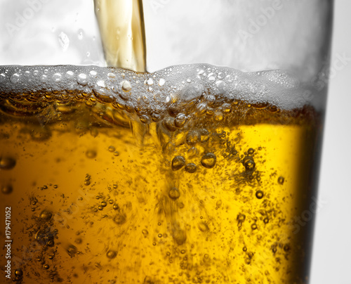 Closeup of beer pour action into clear glass with bubbles, froth and foam