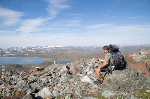 Hiker sitting on a rock and looking at his GPS, Guolasjavri lake, cairn, Summer 