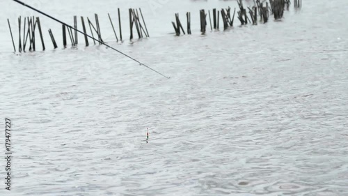 Close-up of a fishing rod of fisherman's on the background of the river and a tany red floater swinging on the waves in a overcast summer day. photo