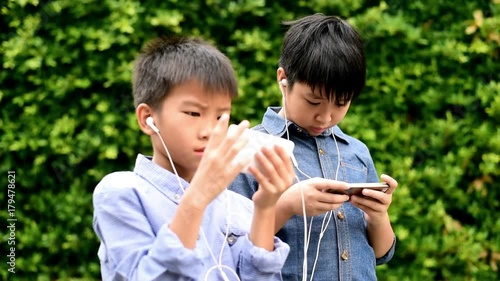 Slow motion of preteen Asian Thai boy is using smartphone to play game in his home garden. Technology and health concept photo