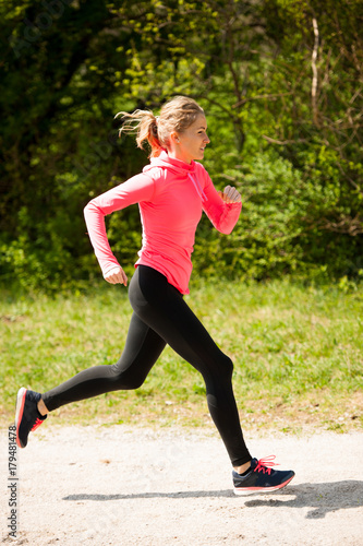 Young woman in pink and black dress runs cross country on a warm spring day