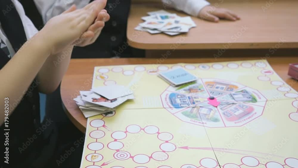 Child plays in kindergarten indoors. Little unknown boy in formal clothes throws a red cube on a card lying on a table. Development game Child plays in kindergarten indoors. Little unknown boy in formal clothes throws a red cube on a card lying on a table. Development game