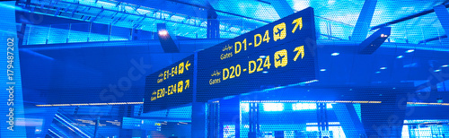 English-arabian yellow illuminated sign at airport with gate letters for departing flights.