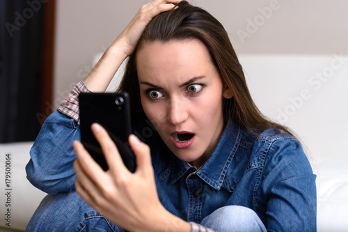 Photos Young woman holding his head and looks to the smartphone