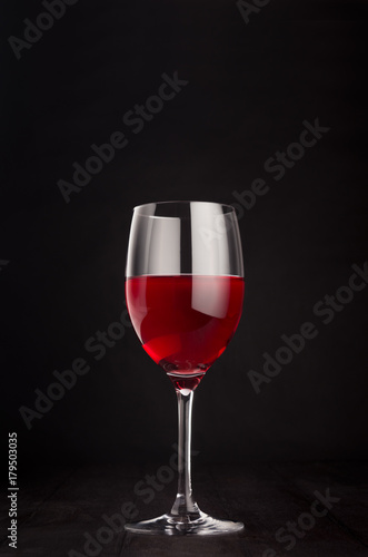 Wine glass with rose wine on elegant dark black wooden background, copy space, vertical. Template for portfolio, advertising, design, branding identity, cover magazine, bar and restaurant menu.