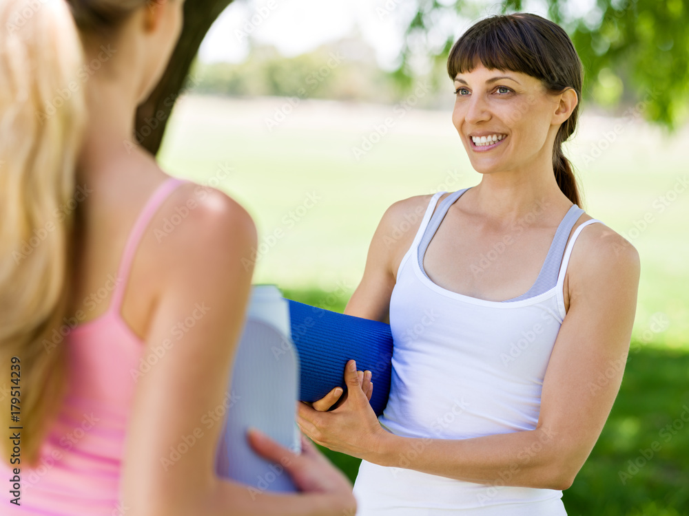 Two young women with a gym mat chatting in the park