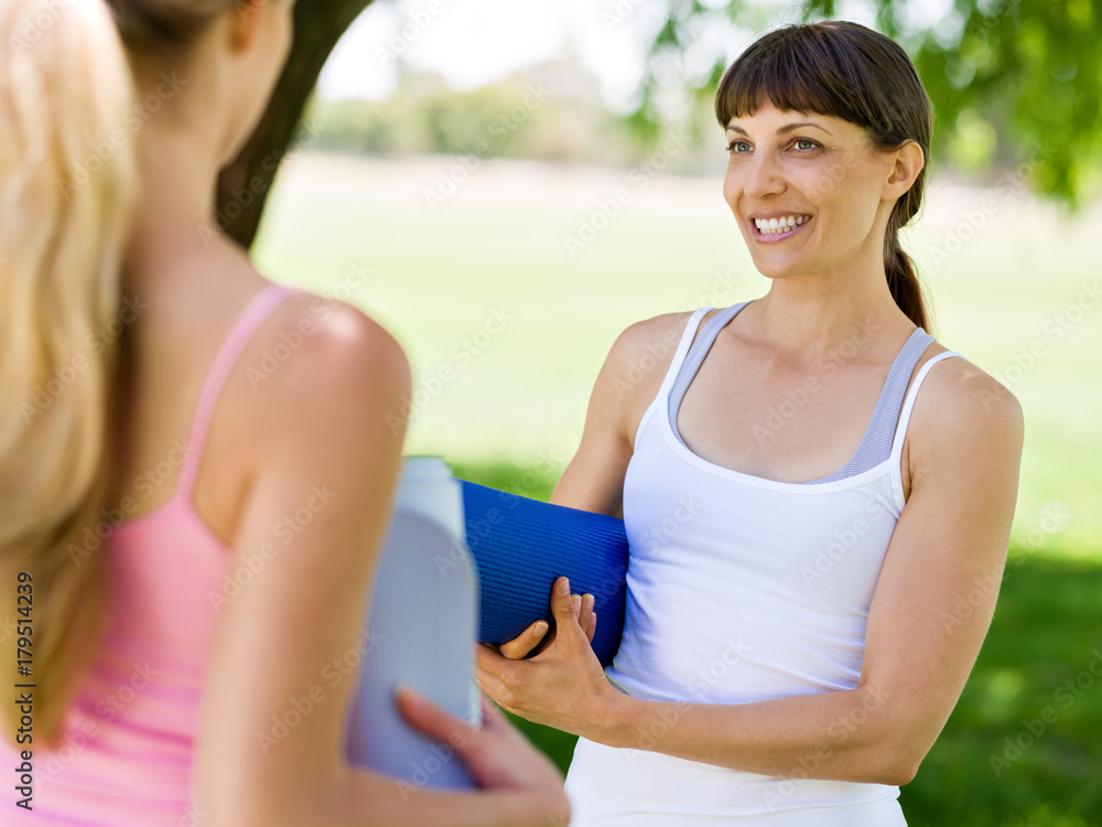 Fototapeta premium Two young women with a gym mat chatting in the park
