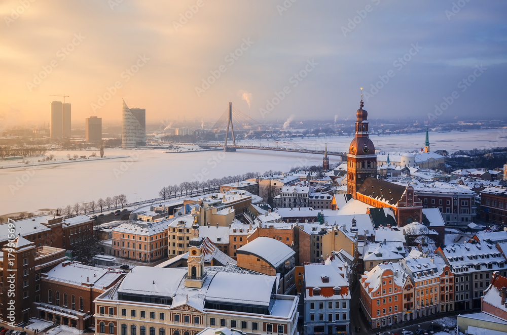 Fototapeta premium View of the roofs of the old city and the tower of the Dome Cathedral against background of an ice-covered river. Winter evening in Riga. Latvia.